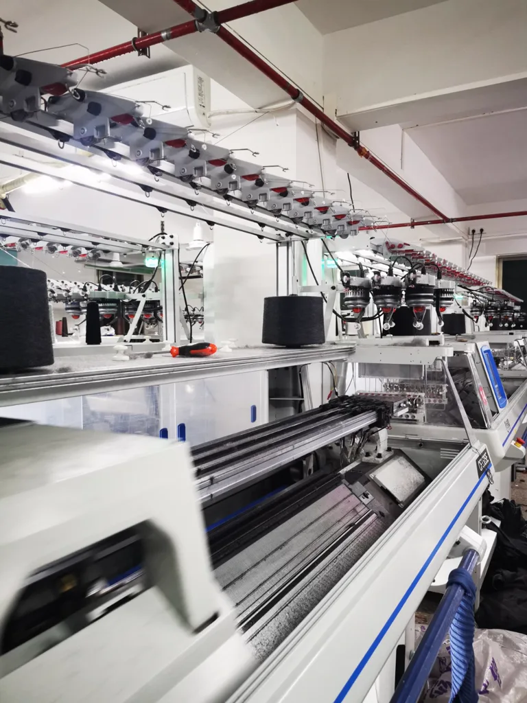 Yarn cones and a row of computerized flat knitting machines in the workshop