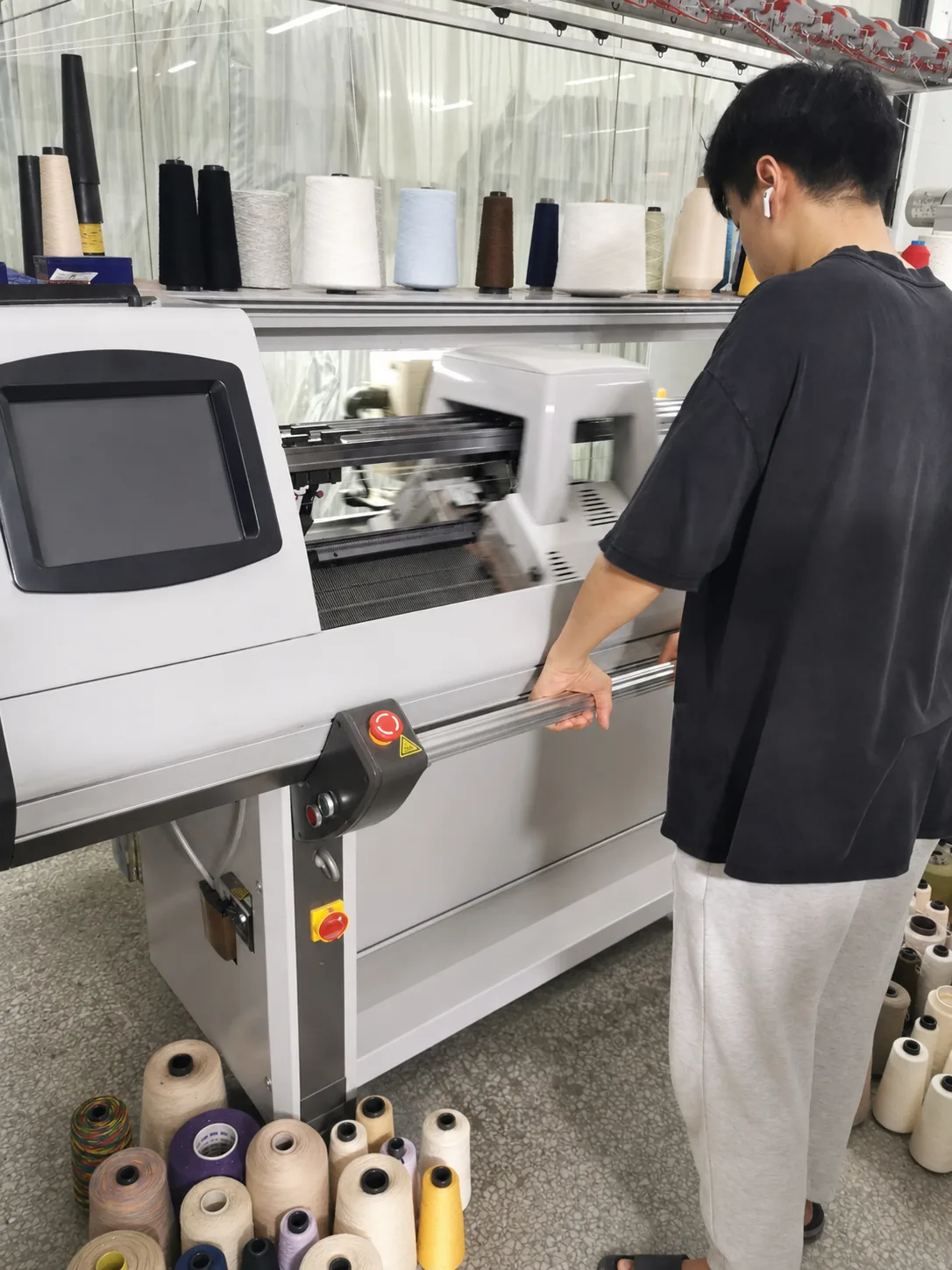 TYKNIT Bediener überwacht eine computergesteuerte Flachstrickmaschine während der Pulloverproduktion