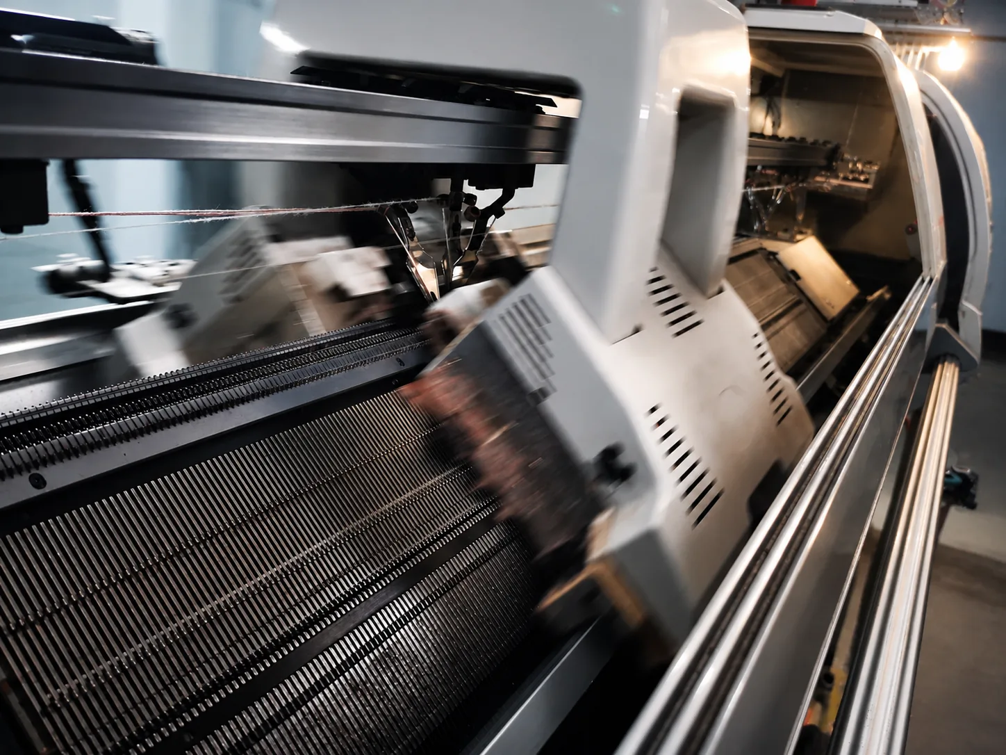 Close-up of a computerized flat knitting machine running during knitwear production at TYKNIT
